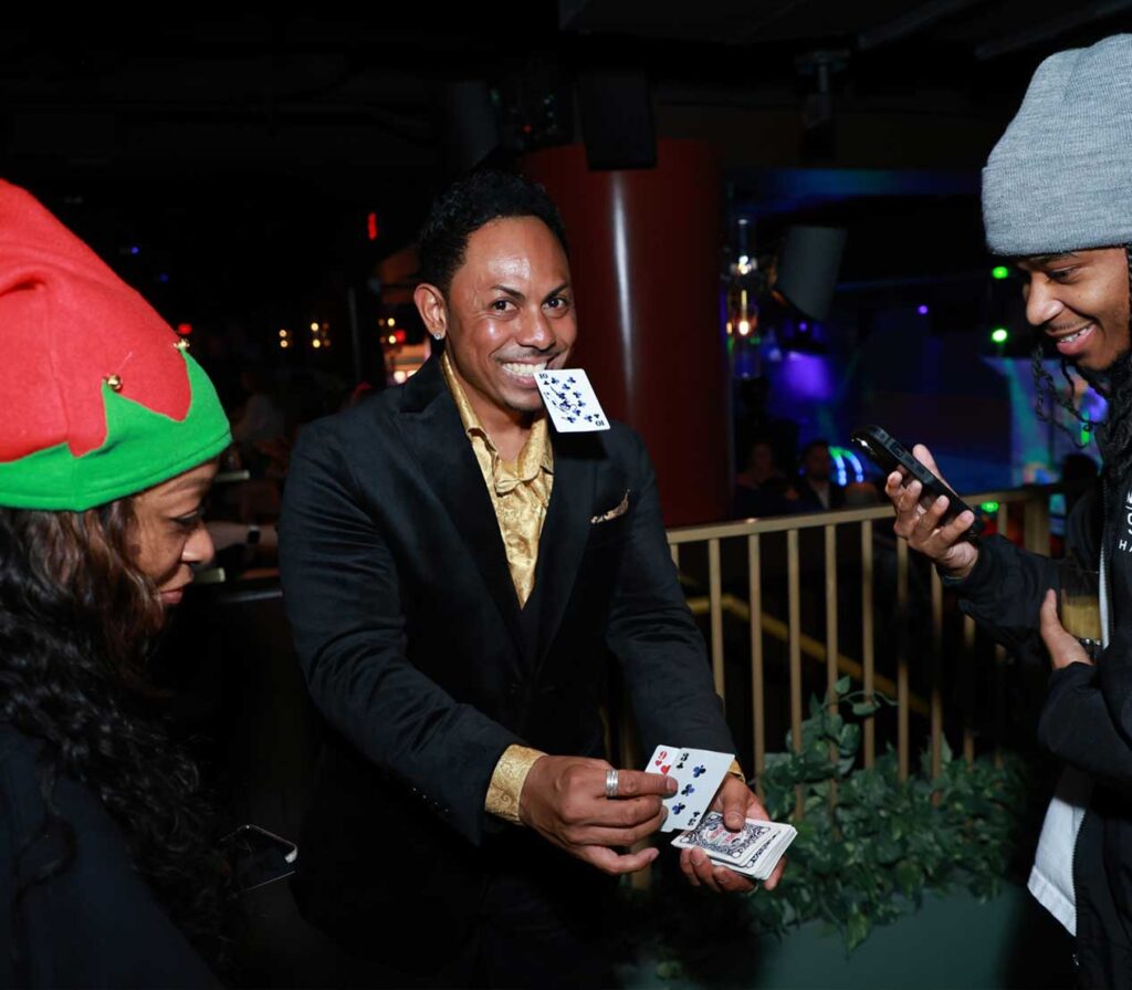 las vegas corporate strolling magician chris workman holding a card in his mouth and showing magic to two people at a corporate event
